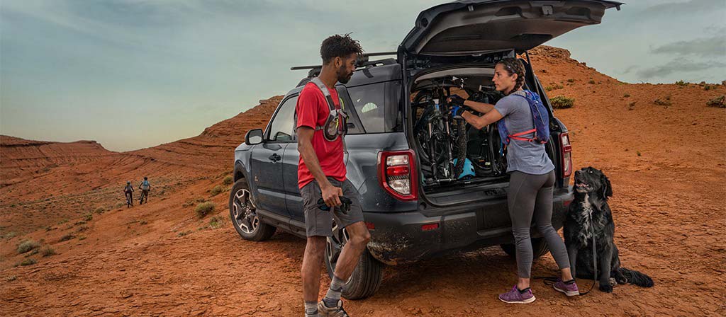 2026 Ford Bronco Sport® SUV parked in the desert with two people standing outside of the vehicle, wearing hiking gear with their dog
