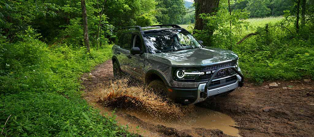 2026 Ford Bronco Sport® being driven on a dirt trail and through a puddle in the woods