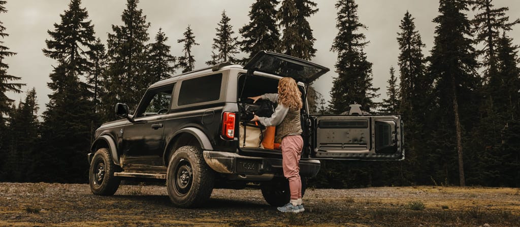 A woman unloading gear from the back of a 2025 Ford Bronco® SUV, showing the side-opening tailgate