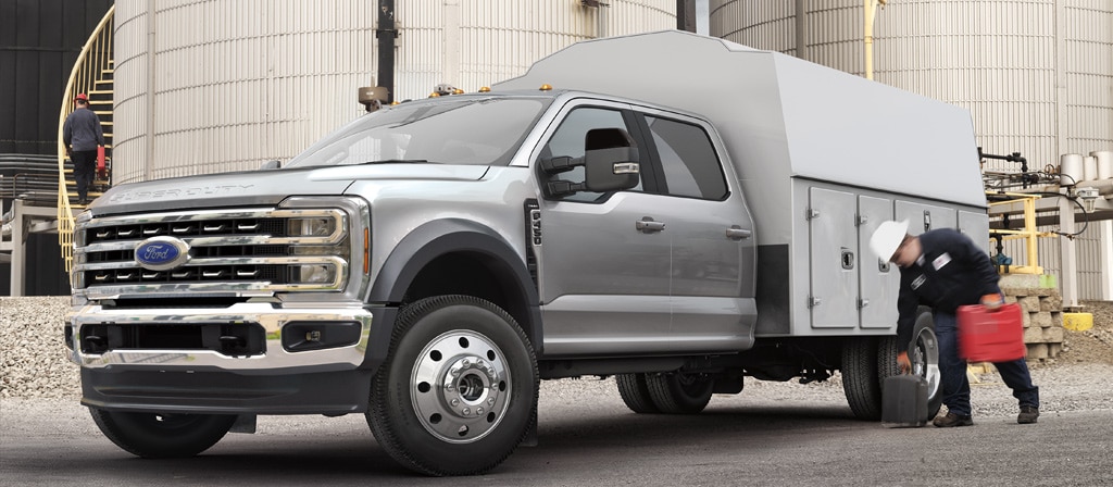 A worker picking up equipment in front of the utility box on their 2026 Ford Super Duty® Chassis Cab