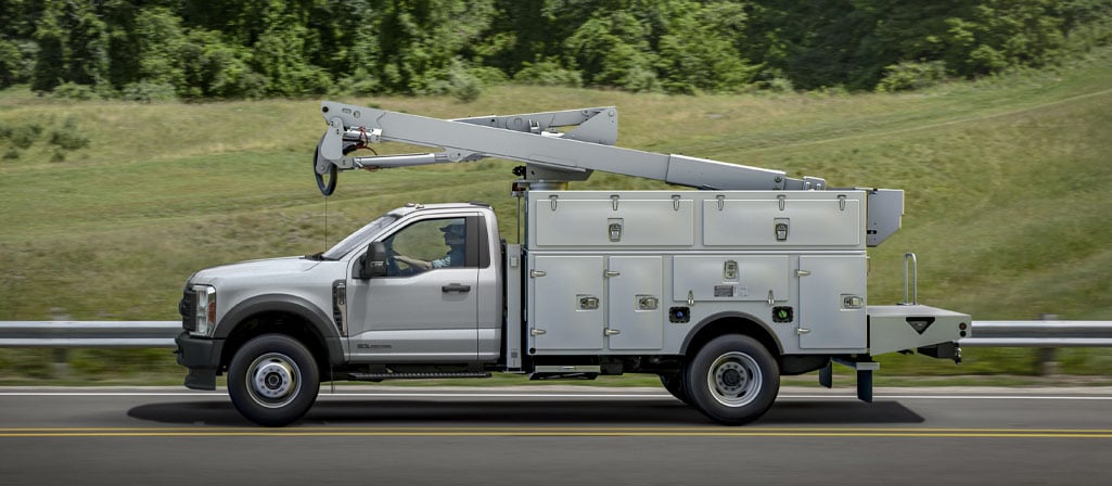 A 2026 Ford Super Duty® Chassis Cab with a boom extension and utility box driving down a road