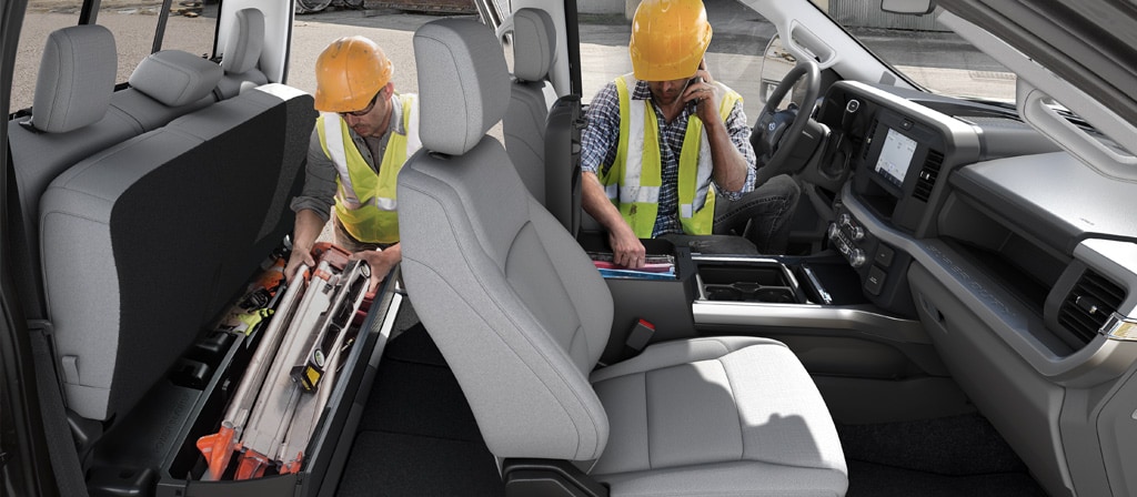 Two workers in hard hats access the storage areas inside the cab of the 2026 Ford Super Duty® Chassis Cab