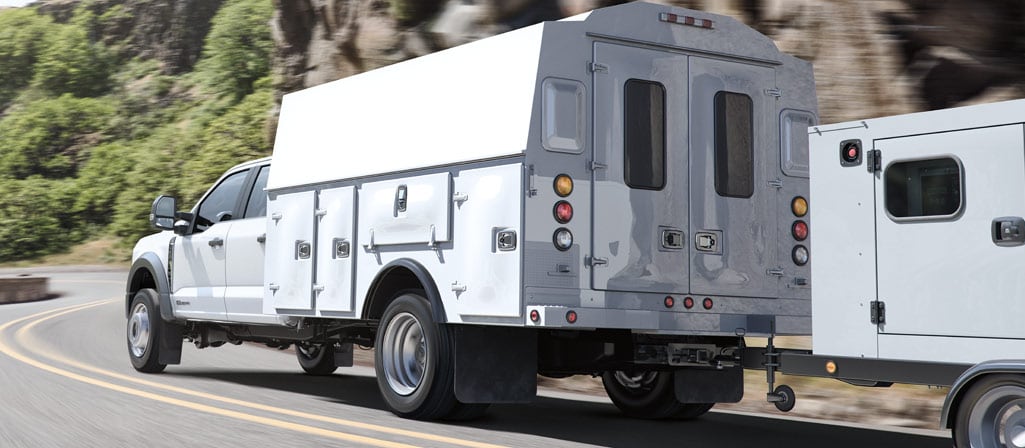 A 2026 Ford Super Duty® Chassis Cab with a utility box being driven up a road alongside a mountain