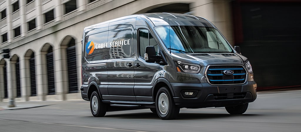 A blue 2025 Ford E-Transit™ van being driven down a city street