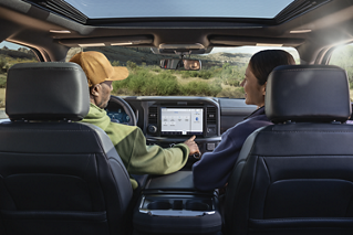 Man using the push-button features on the 12-inch centre display with a woman seated in the passenger seat