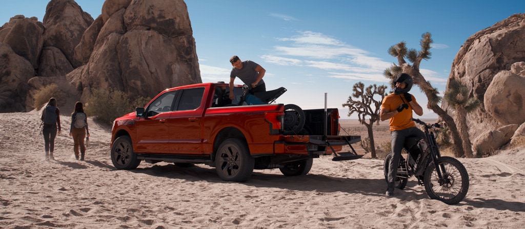 People near a 2025 Ford F-150® Lightning® pickup in the desert, with a dirtbike in the bed and one unloaded