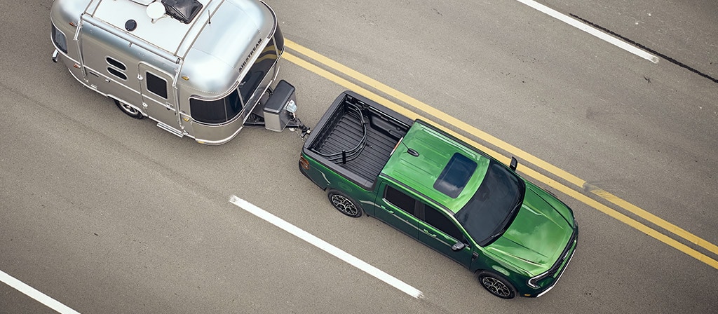 An aerial view of a 2025 Ford Maverick® pickup pulling a travel trailer down a highway