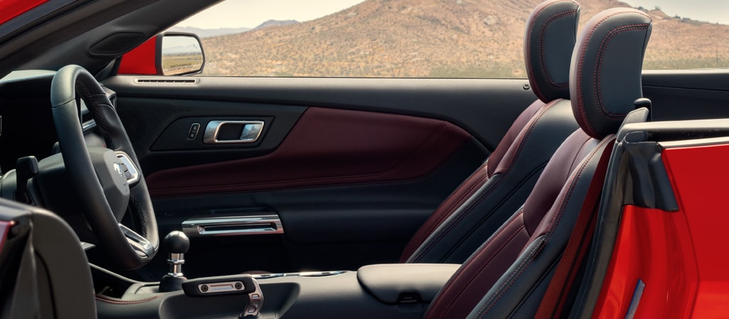 Parked 2026 Ford Mustang® convertible with the driver's side door open showing the available Carmine Red interior