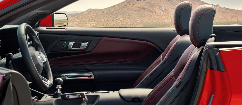Parked 2026 Ford Mustang® convertible with the driver's side door open showing the available Carmine Red interior