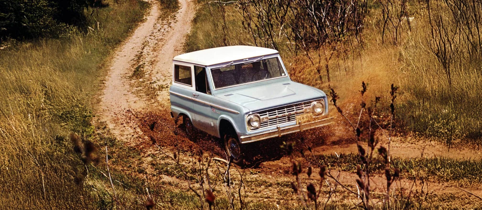 1960s Bronco Wagon driving down a dirt road.