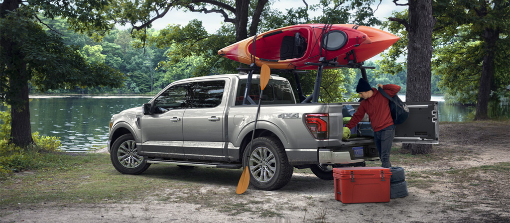F-150 parked near a lake with mounted canoe and a person unloading gear from the bed.