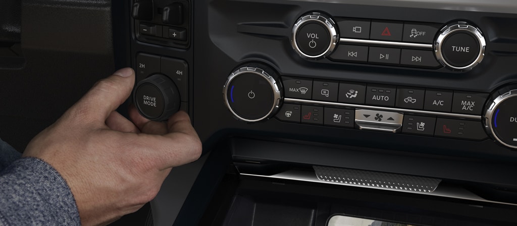 A person's hand using the Drive Mode knob of a 2026 Super Duty® truck with a phone being charged on the wireless charging pad