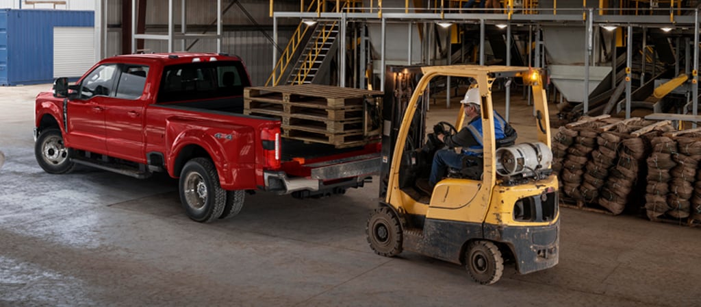 2026 Ford Super Duty® F-350® Lariat® model with the tailgate open while a forklift loads wooden palettes into the truck bed