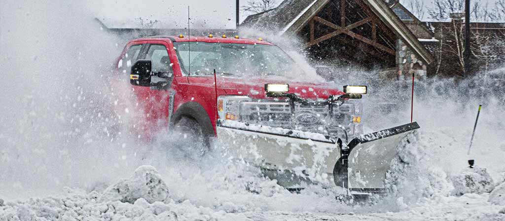2026 Ford Super Duty® F-450® XLT truck in Race Red driving through heavy snow with snowplow equipment
