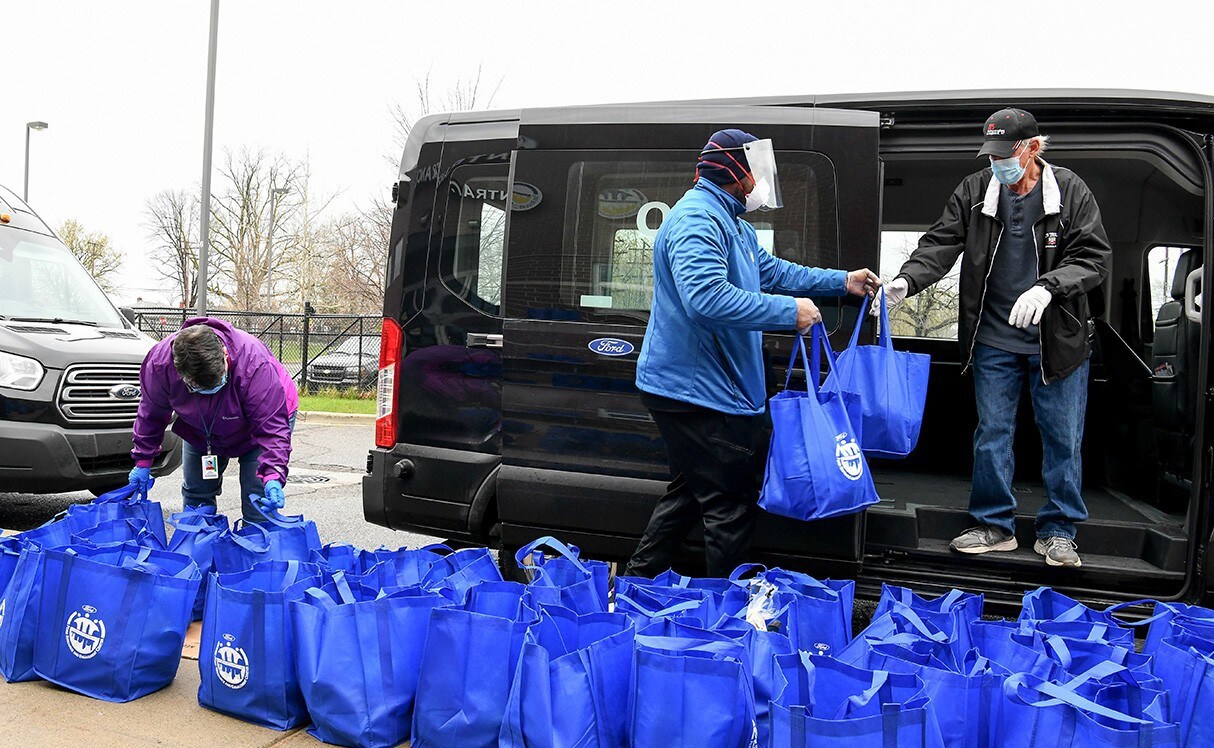 People putting blue bags into a Ford Transit van