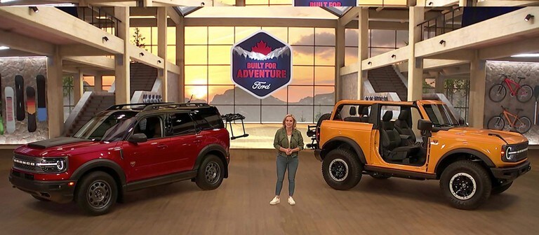 A woman stands between a red 2021 Ford Bronco and a yellow 2021 Ford Bronco Sport