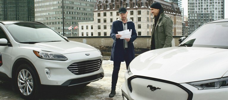 Two men stand next to a white 2021 Ford Mustang Mach e