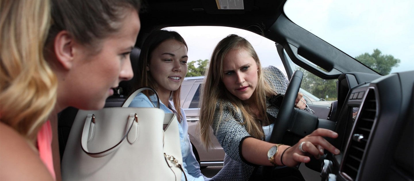 Three women exploring the dashboard controls of a Ford vehicle.