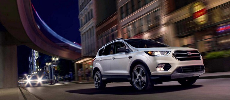 A Ford Escape drives along a city street at night