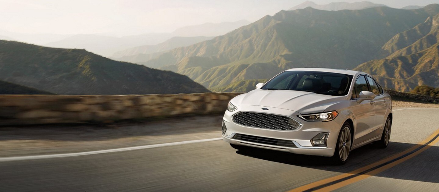 A white Ford Fusion driving on a mountain highway