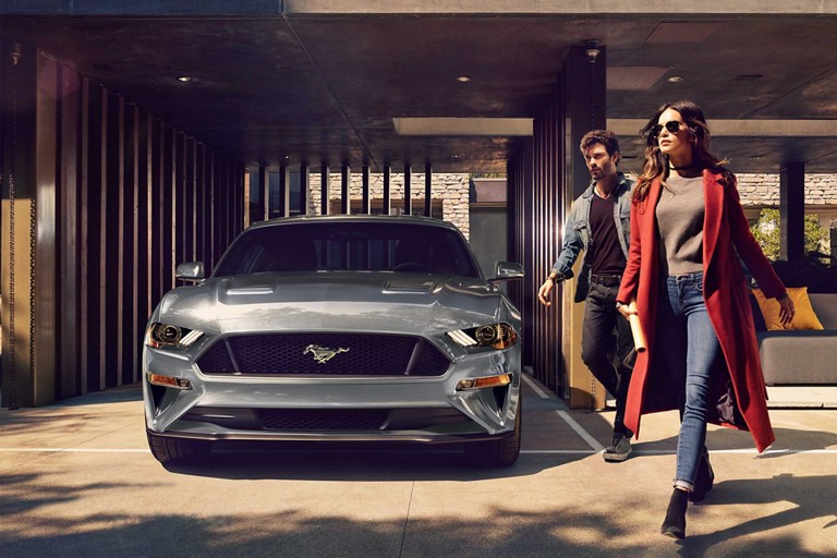 2023 Ford Mustang® coupe in Carbonized Grey Metallic parked in a carport with two people walking away