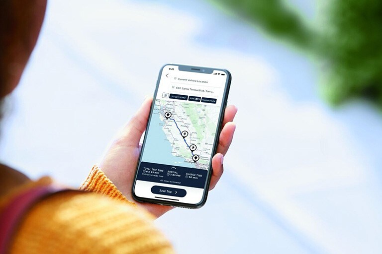 A hand holds a smart phone showing a map diplaying the location of charging stations