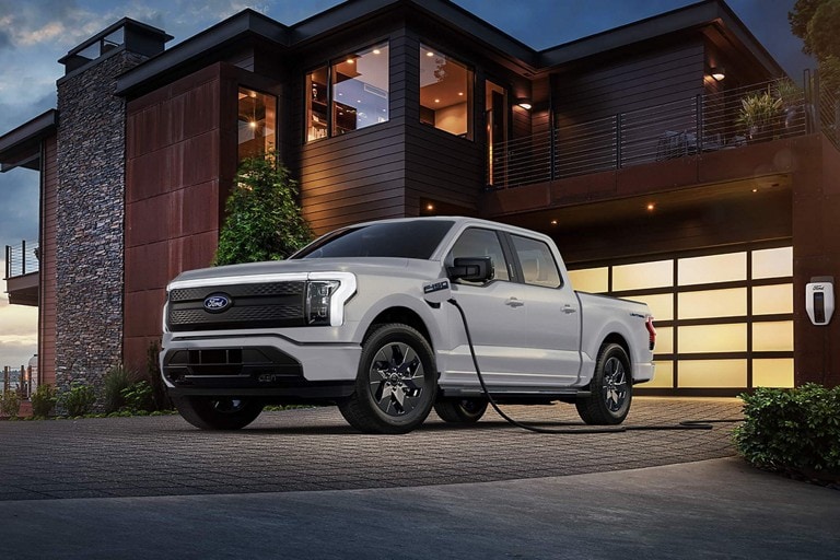 F-150 Lightning parked in front of a home and plugged into a Ford Charge Station Pro.