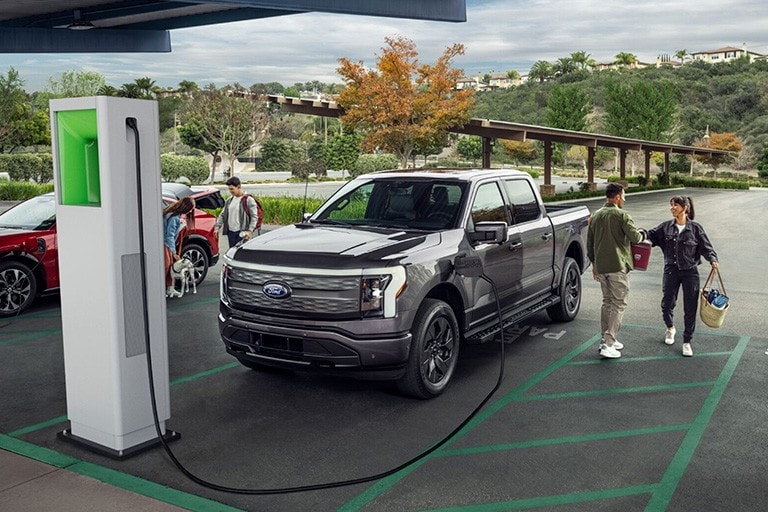 A couple stand next to a Ford F 1 50 Lightning parked at a D C fast charging station