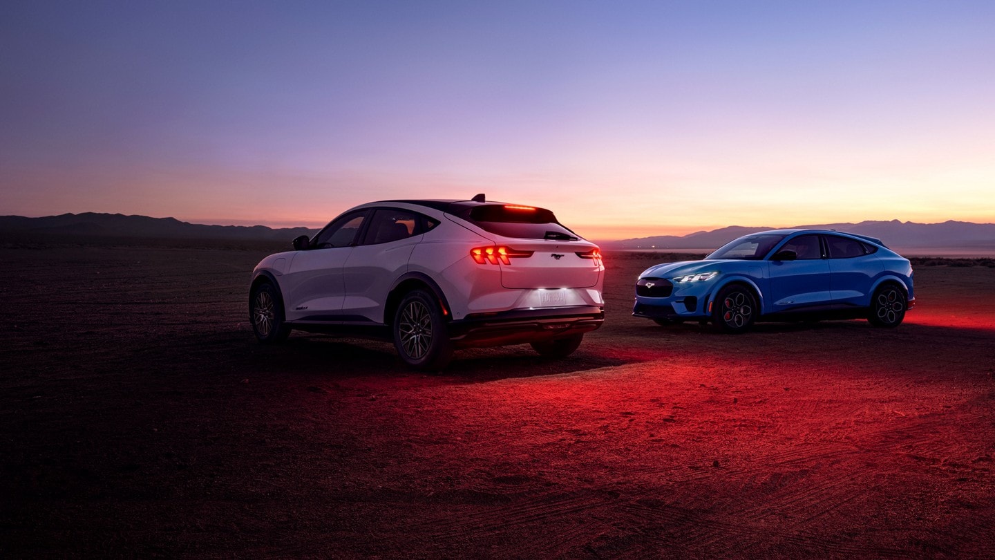 A silver and blue Mustang Mach E are parked side-by-side in a desert setting
