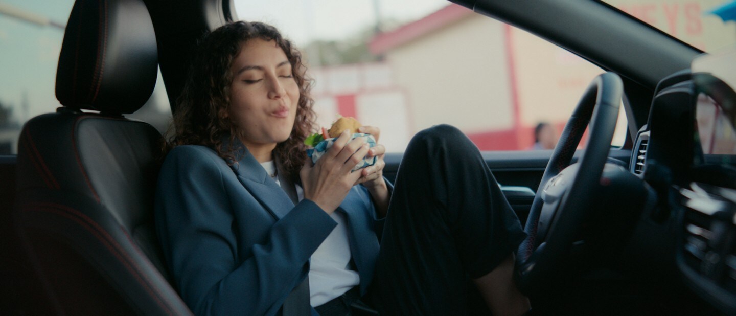 A woman eating a burger inside a 2023 Ford Escape. 