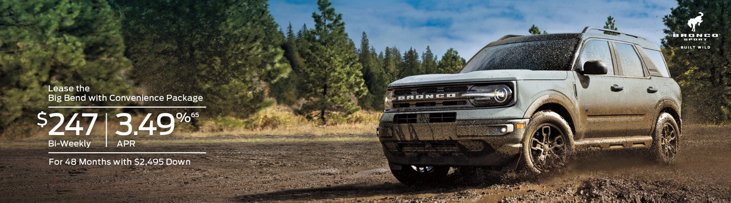Lease the Big Bend with Convenience Package for $247 Bi-Weekly. 3.49%65 APR for 48 Months with $2,495 Down. A muddied white 2023 Ford Bronco Sport drives on a dirt track with evergreen trees in the background.