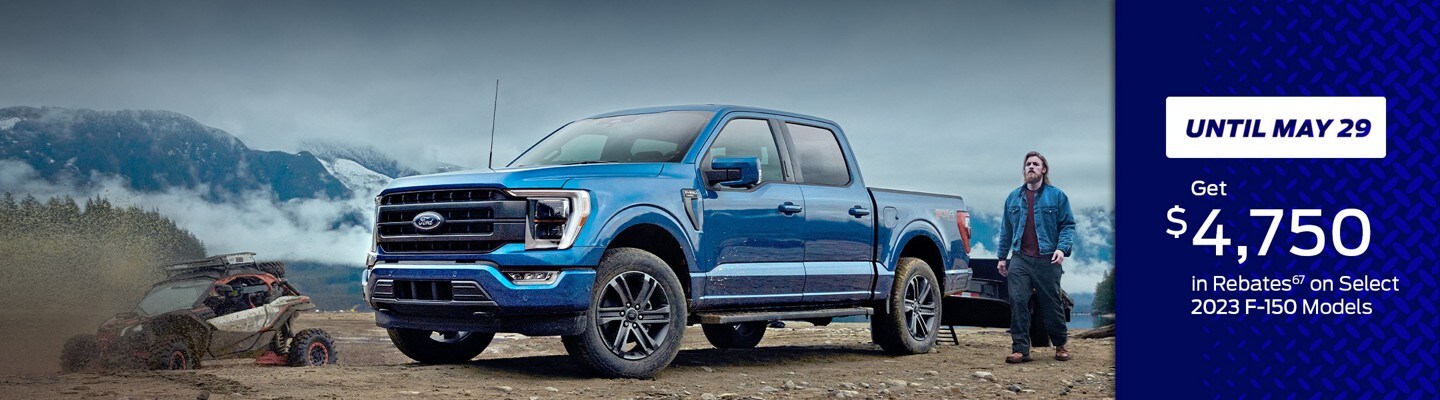 Until May 29 Get $4,750 in Rebates 67 On Select 2023 F-150 Models. A man stands next to a blue 2023 Ford F-150 with two muddy adventure vehicles nearby. Snowy mountains loom in the background.