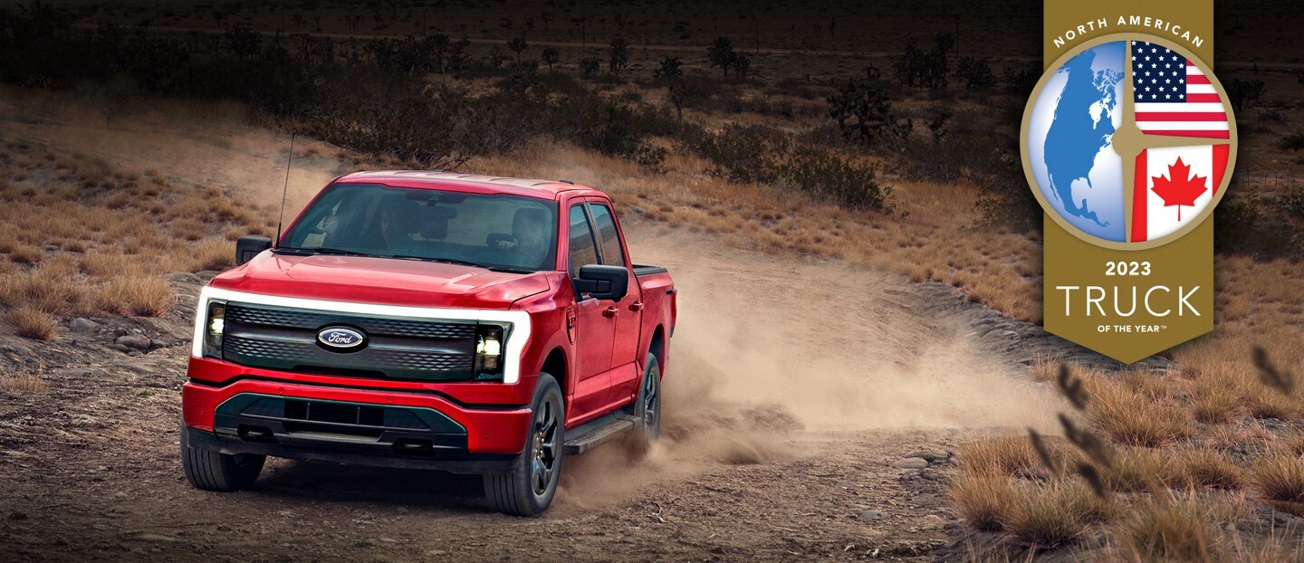 A red 2023 F-150 lightning is driving through a dessert setting with a "2023 North American Truck of the Year" award on the top right corner. 