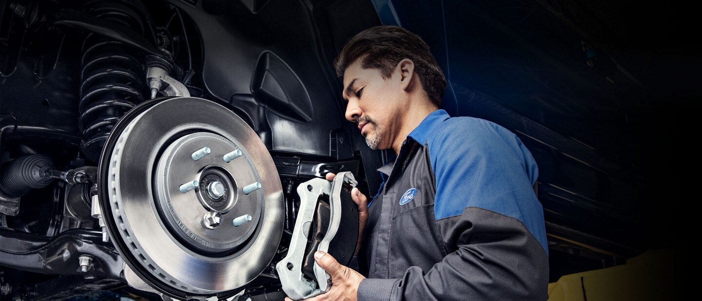 A Ford technician installs brake calipers on a rotor
