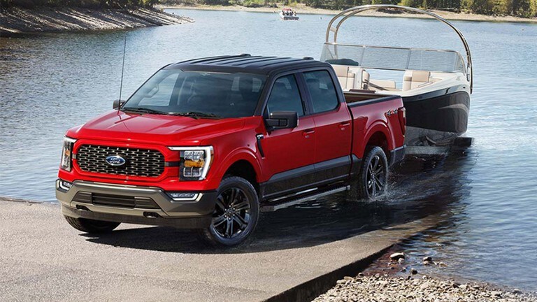 A red 2023 Ford F-150 Heritage Edition pulling a boat out of a lake.