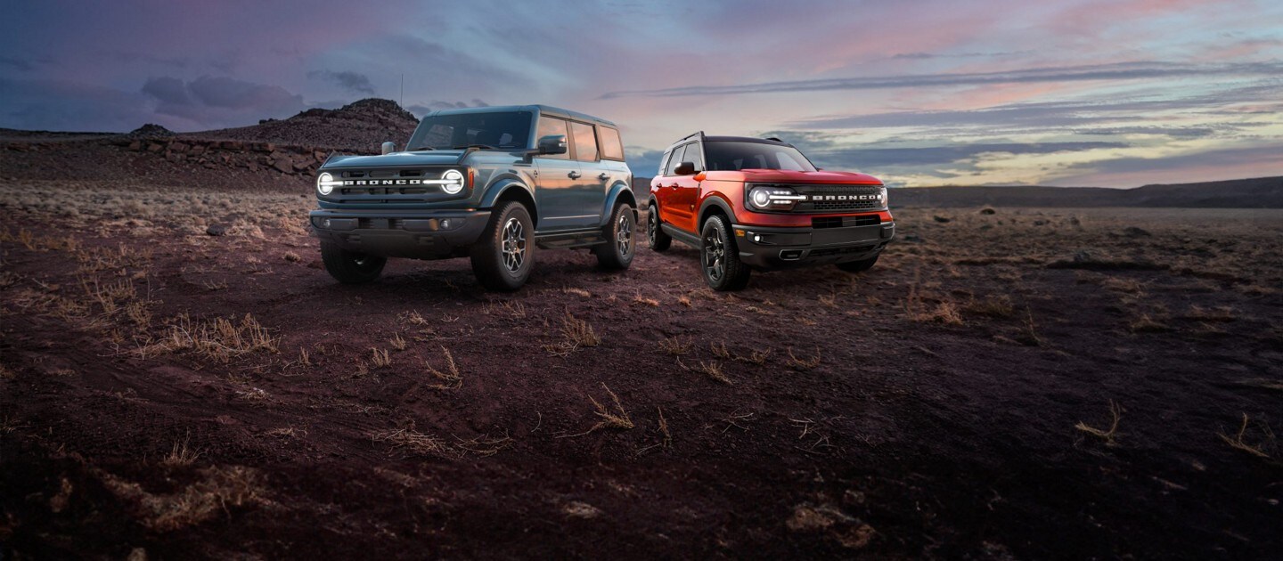 A blue 2024 Bronco and a red 2024 Bronco Sport parked on a tundra landscape at dusk.