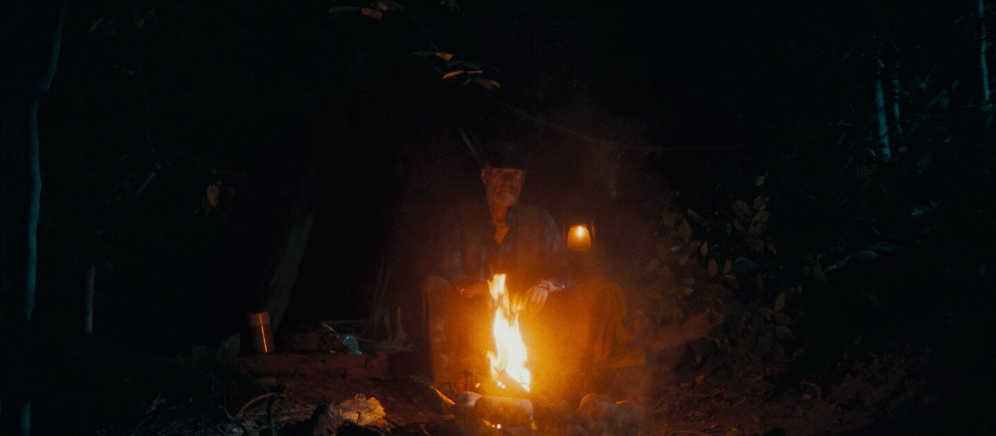 An old man sits by a fire, surrounded by darkness