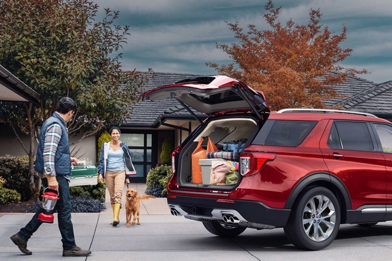 A couple with dog walk towards a Ford SUV.