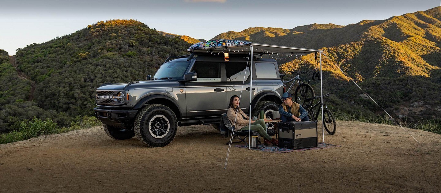 A Ford Bronco Sport is parked on a trail. A couple is walking their bikes away from it.