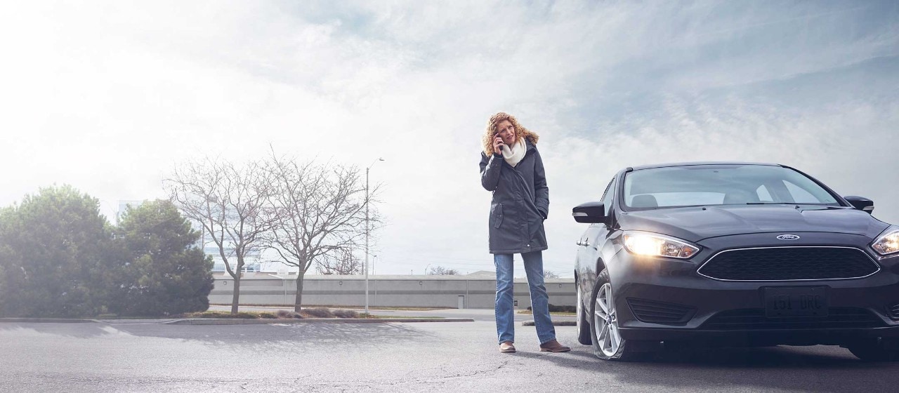 A woman standing beside her car, making a phone call