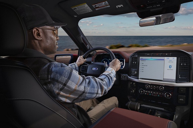 A person drives a Ford vehicle while a shopping list is displayed on the SYNC screen