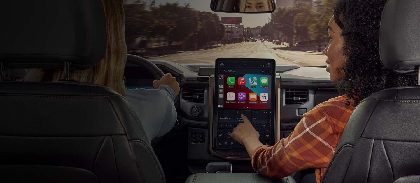 A person in the passenger seat touches the a SYNC screen displaying Apple CarPlay