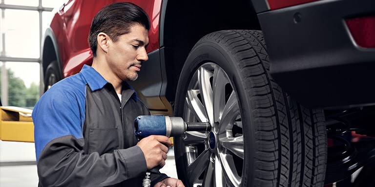 A Ford service technition uses a pneumatic wrench on a wheel