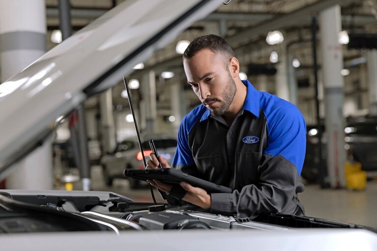 A Ford technician inspects an engine with a checklist.