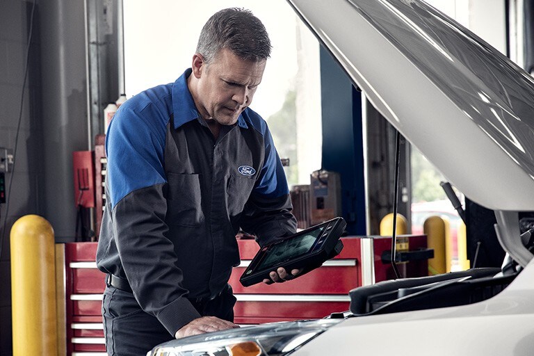 A Ford technician inspects an engine holding a tablet computer