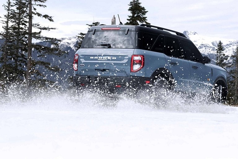 A blue Ford Bronco driving through snow