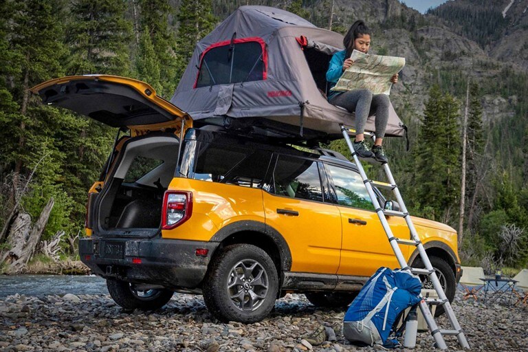 A woman sits in an available tent pitched atop a yellow Ford Bronco.