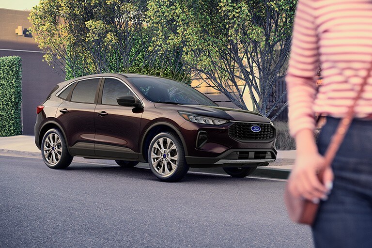 A woman walks away from a black 2023 Ford Escape parked on a city street