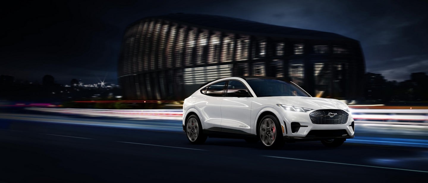 A White Ford Mustang Mach-E races along a highway at night.
