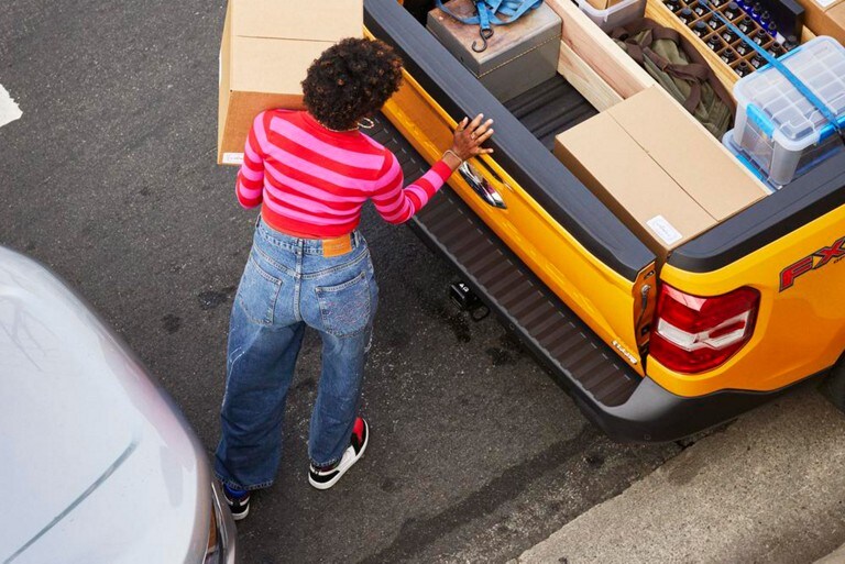 A woman loads cargo into the rear of a Ford Maverick